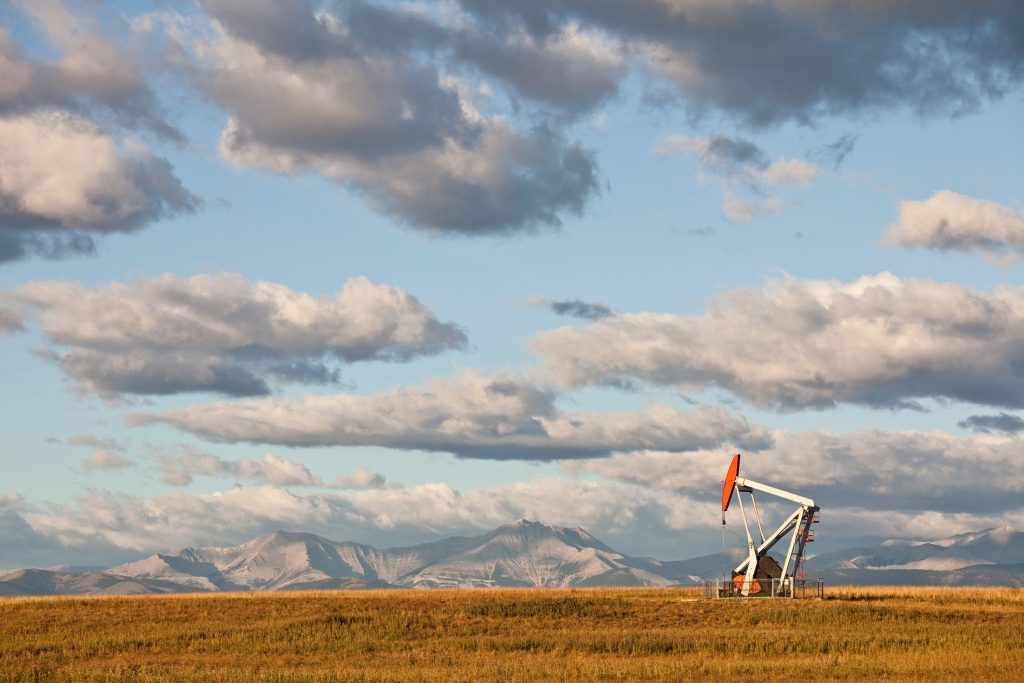 A pumpjack on the prairie. Alberta, Canada.Rocky Mountains in distance. Crude oil and the oil industry in general is a huge industry in Western Canada. Additional themes here include natural gas, fossil fuel, energy, gas, power, scenic, landscape, oil field, oilsands, pipeline, oil rig, geology, engineering, and fracking.